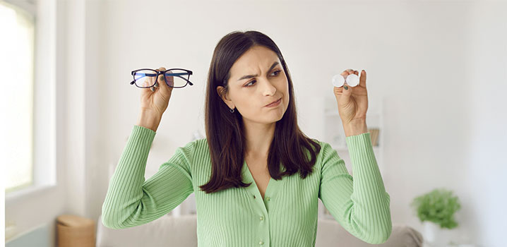 Junge Frau hält eine Brille und einen Kontaktlinsenbehaelter hoch