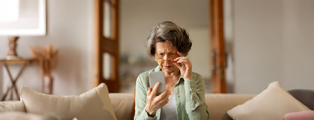 Alte Frau mit Brille sitzt auf Sofa und hält Smartphone in der Hand