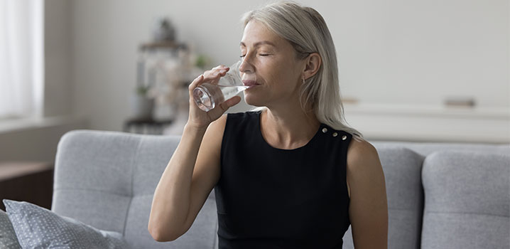 Frau im schwarzen Oberteil trinkt ein Glas Wasser