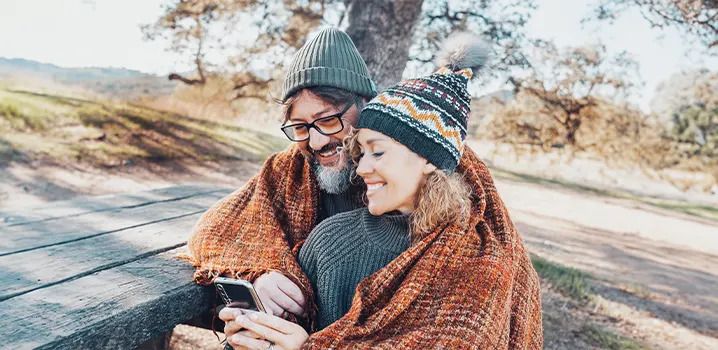Mann und Frau sitzen gemeinsam unter einer Decke auf einer Bank im Freien