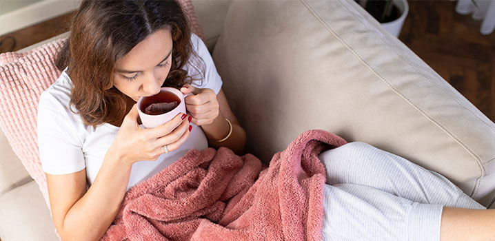 Frau liegt auf dem Sofa und trinkt Tee