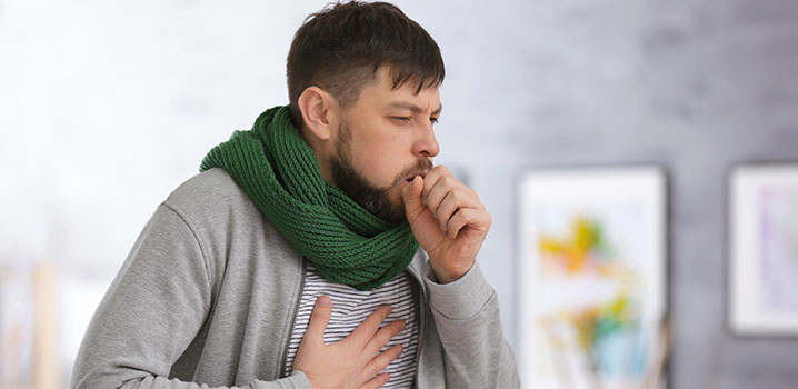 Mann mit Schal hustet und hält sich die Brust