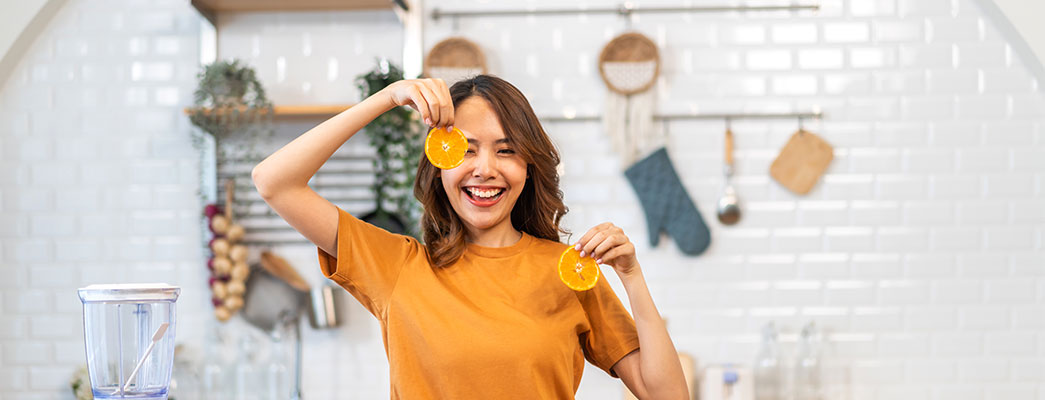 Junge Frau steht in der Küche und hält Orangenscheiben in der Hand