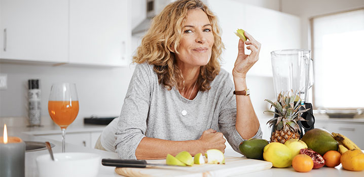 Blonde Frau sitzt am Küchentresen und isst einen Apfel