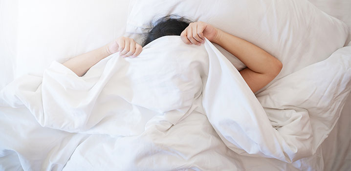 Frau zieht sich im Bett die Decke über den Kopf