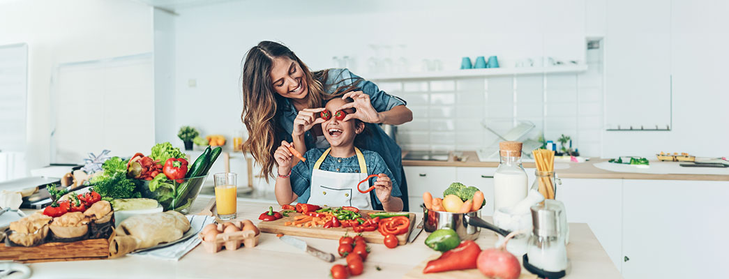 Mutter hält Tochter beim gemeinsamen Kochen Tomaten vor die Augen