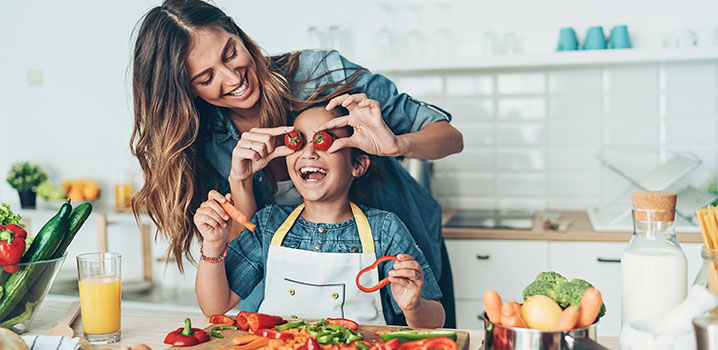 Mutter hält Tochter beim gemeinsamen Kochen Tomaten vor die Augen