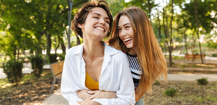 Zwei junge Frauen gehen im Park spazieren und lachen zusammen