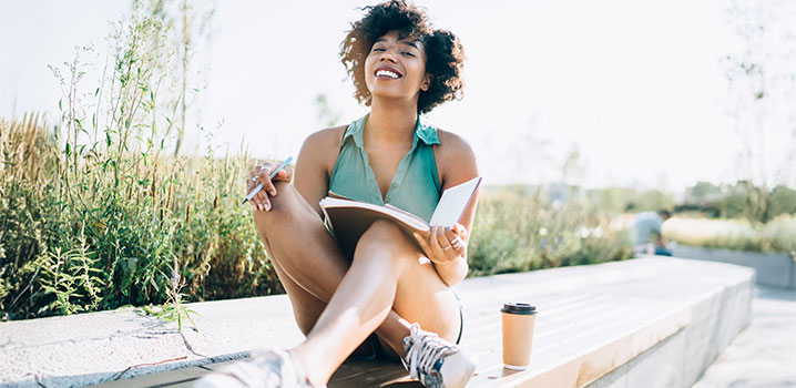 Junge Frau sitzt im Sommer auf einer Bank und lernt