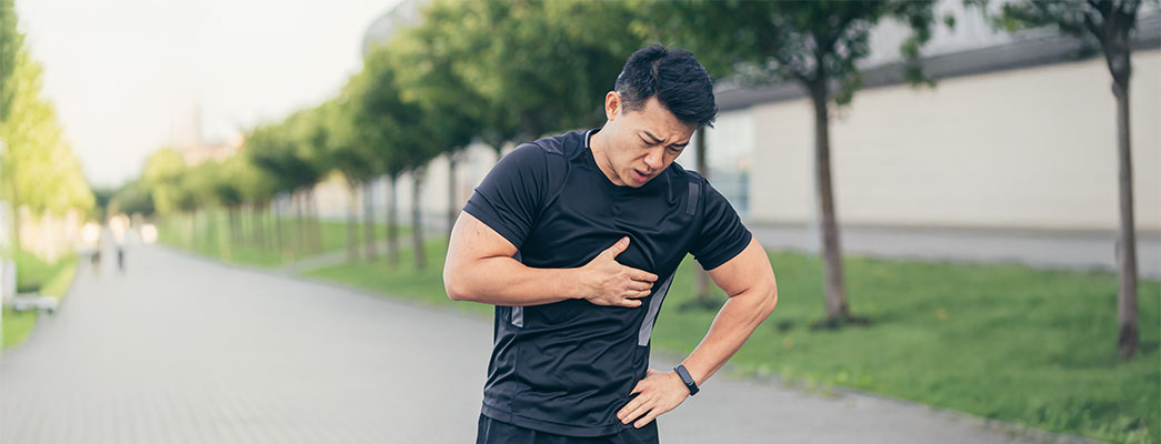 Junger Mann in Sportkleidung fasst sich an die Brust