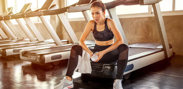 Junge Frau sitzt ausgepowert auf einem Laufband im Fitnessstudio