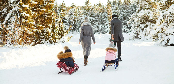 Vater und Mutter ziehen zwei Kinder in Schlitten durch den Schnee