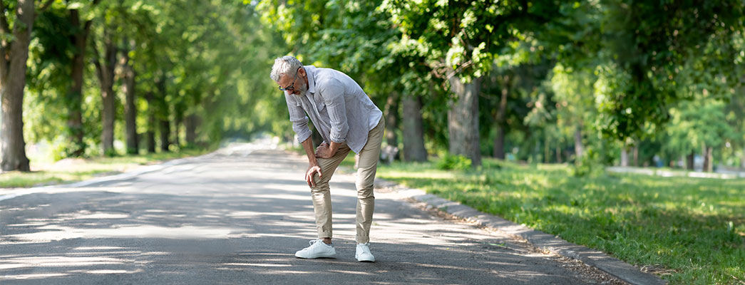 Älterer Mann steht auf einem Spaziergang und hält sich das Knie