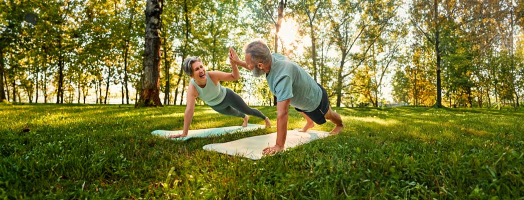 Zwei Senioren auf Yoga–Matten geben sich ein High–Five