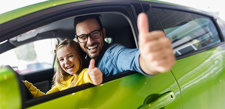 Vater und Tochter sitzen zusammen im Auto und strecken die Daumen aus dem Fenster