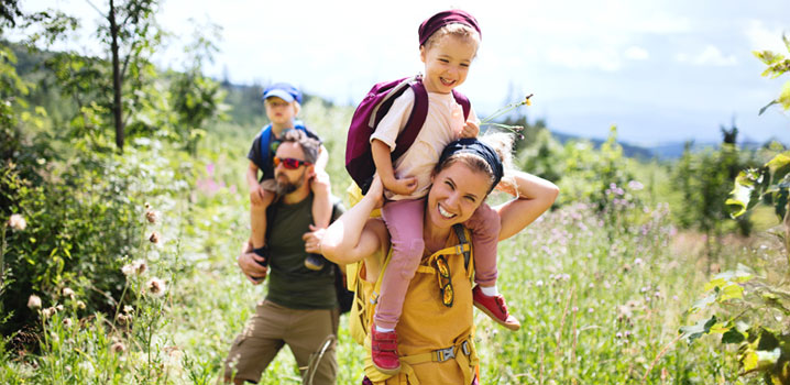 Mutter und Vater mit Kindern auf den Schultern wandern durch die Natur