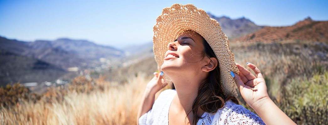 Junge Frau mit Strohhut hält ihr Gesicht in die Sonne